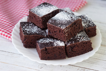 Chocolate cake cut into square pieces, sprinkled with icing sugar on a plate, white background