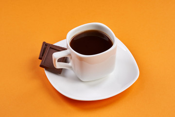 Cup of coffee with chocolate bars on orange background