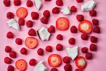 Many raspberries, strawberries and coconut pieces on pink background