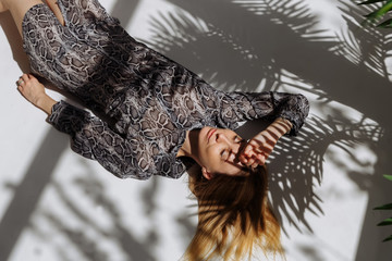 A girl in a gray dress lies in the shade of plants with her eyes closed. Fashion photography in a photo studio. A shadow falls on a white background.