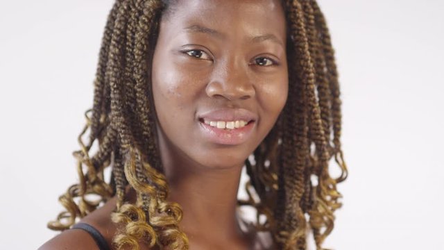 Tilt up portrait shot of young African-American woman with dreadlocks standing isolated on white background and putting a bit of moisturizing face cream on her cheek, then smiling for camera
