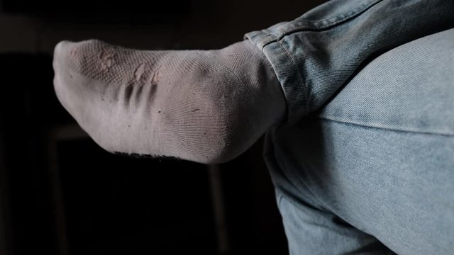 Foot of Lonely Untidy man sitting at home with a holey dirty old white sock..