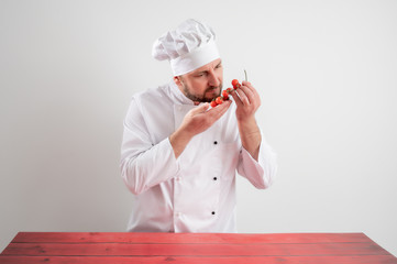Young male chef in white uniform smell tomato