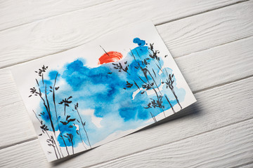 High angle view of paper with japanese painting with blue sky, branches and sun on wooden background