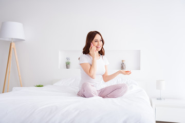 Portrait of her she nice attractive lovely pretty friendly cheerful cheery red haired girl sitting in bed talking on phone in modern white light interior style room house apartment indoors