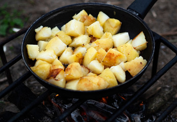 Potatoes are fried in a pan mounted on a wire rack over a fire.
