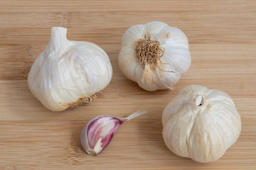 3 pieces of white garlic bulbs and one clove on light brown wooden chopping board. Garlic for use as seasoning and for health benefits. Selective focus.