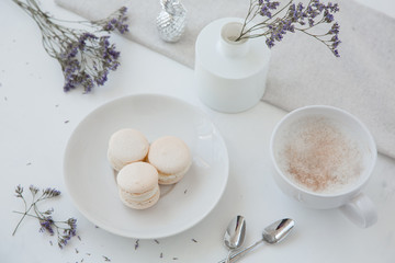 Fototapeta na wymiar Macarons, morning coffee on light table from above flat lay with blurred vase and blue flowers on background