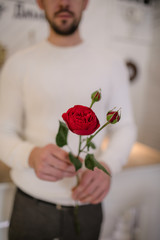 Man in white sweater holding vase with peonies inside the room