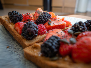 Toast on a plate with Peanut butter, strawberries, blackberries, chai seeds and pumpkin seeds. Close up. 