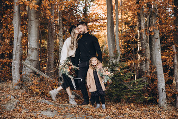 Stylish family in the autumn forest. A young guy and a girl are standing near a wooden fence with...