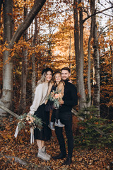 Stylish family in the autumn forest. A young guy and a girl are standing near a wooden fence and holding their daughter in their arms. Mom and daughter are holding bouquets of flowers