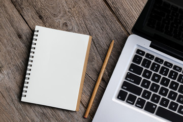 Blank notebook with laptop beside on wooden table