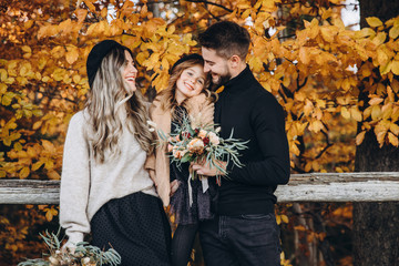 Stylish family in the autumn forest. A young guy and a girl are standing near a wooden fence and holding their daughter in their arms. Mom and daughter are holding bouquets of flowers