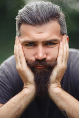 Fototapeta premium tired brutal bearded man with gray hair in his hair sits propping his hands on his face