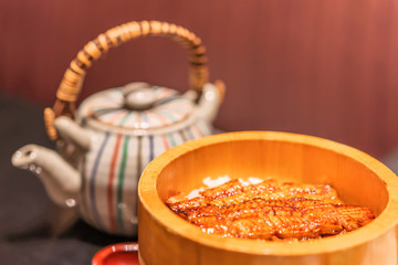 Fillets of japanese unagi eel  grilled in a kabayaki style in a wooden bowl with a tea-pot .