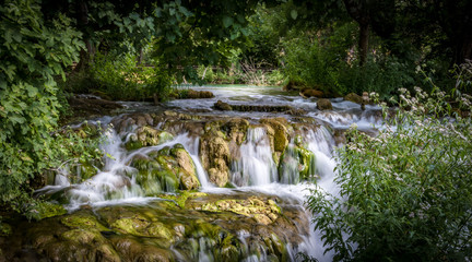 tranquil little long exposure waterfall in a green foliage woodland at spring time
