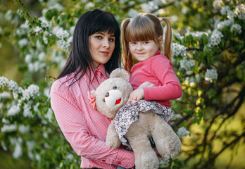 A little girl in her mother's arms in a park near a flowering tree