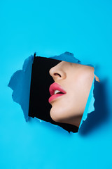 Female face with pink lips in hole in blue paper on black