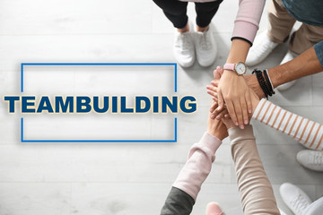 People holding hands together over wooden background, closeup. Teambuilding concept