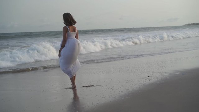 Playful beautiful woman dancing with a white dress on the shore of the ocean beach