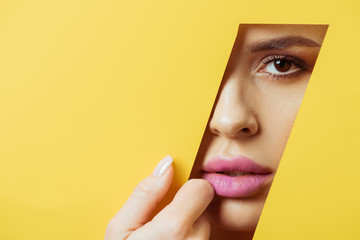 Woman with pink lips looking at camera across quadrangular hole and touching yellow paper