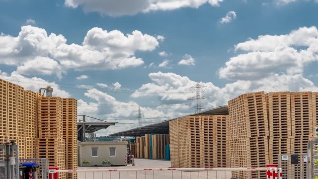 Time lapse of a pallet factory with movement of people and goods against a beautiful sky and moving white clouds