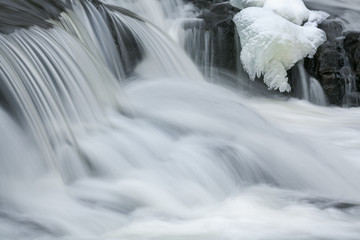 Winter landscape of a cascade at Bond Falls captured with motion blur and framed by ice and snow, Michigan's Upper Peninsula, USA