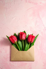 Bunch of red tulip flowers in paper envelope on textured pink background, top view copy space