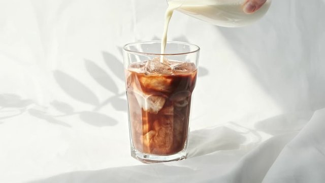 Milk cream is poured into a iced coffee cold brew.  Coffee cold drink with ice and milk.