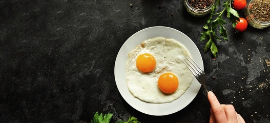 Fried eggs in a white plate. Beautiful fried eggs. Tasty breakfast. Top view, dark concrete background. Free space for text