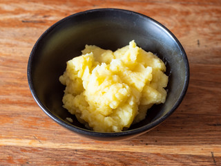 portion of mashed potatoes in black ceramic bowl on old wooden table in home kitchen