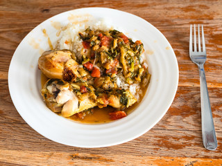 cooked Chakhokhbili (traditional georgian dish from stewed chicken, tomato, eggplant and fresh herbs) with boiled rice on white plate on old wooden table in home kitchen