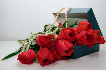 A bouquet of red flowers lies in a gift box with pearls.
