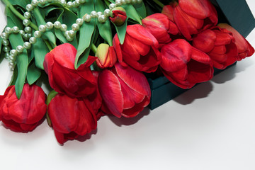 Red tulips lie on a white surface with pearls. A beautiful bouquet for a holiday.