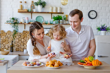 Family portrait of a happy mother, daughter and father posing in the kitchen during Breakfast, eating delicious macaroons, cakes, cookies. Married good relations, love each other