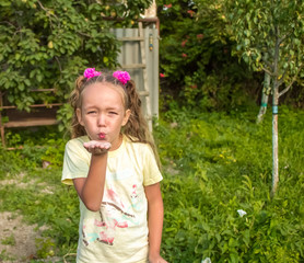 a little girl in a light t shirt stands in the garden in nature and blows a kiss