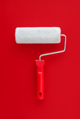 White paint roller with a red handle on a red background. Paint concept