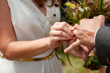 Young bride put wedding ring on the groom's finger with difficulties, close-up. Wedding ceremony, hardly exchanging. Future husband wearing a wedding ring. Swollen finger.