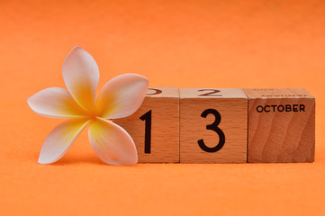 13 October on wooden blocks with a Frangipani flower on an orange background