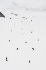 Lots of freeride skiers and snowboarders, large group, rolls and rides on snow slope, and enjoy in the beautiful Alps mountain range. Top high perspective view. Winter season. French Alps, Les 2 Alpes
