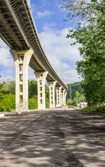 Viaduct, view from below. Construction of the air road. High concrete pillars. Around the spring green nature, the highway.