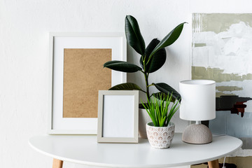 green plants, frames and lamp on white coffee table near painting in modern apartment