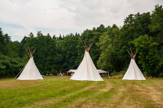 Beautiful view of three tipi tents in a field. Tee pee built on green grass. Traditional teepee tent wigwams located in nature. Czech countryside. Summer wedding.