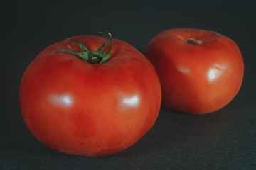 Two ripe red tomatoes on a dark background close-up.