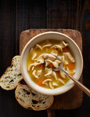 Overhead view of chicken noodle soup with rustic bread on a wooden surface with copy space