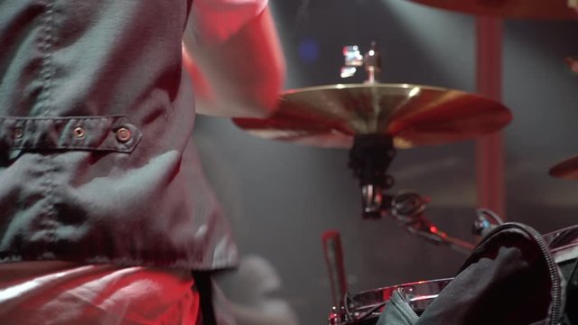 The drummer is actively playing a musical instrument during a live classic rock concert. A man with a drum and sticks. Scene and flashes of light.