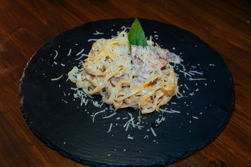 delicious Italian pasta with cheese, seafood, bacon, sausage on a black stone with Basil