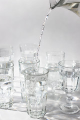 Hand pours fresh water from a decanter into a glass, light background. Close up, vertical.