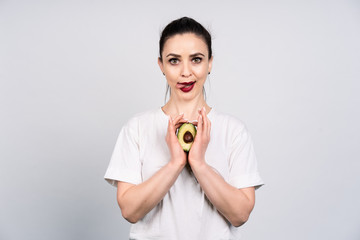 Cute girl in white shirt on gray background keeps the cut avocado, a little language